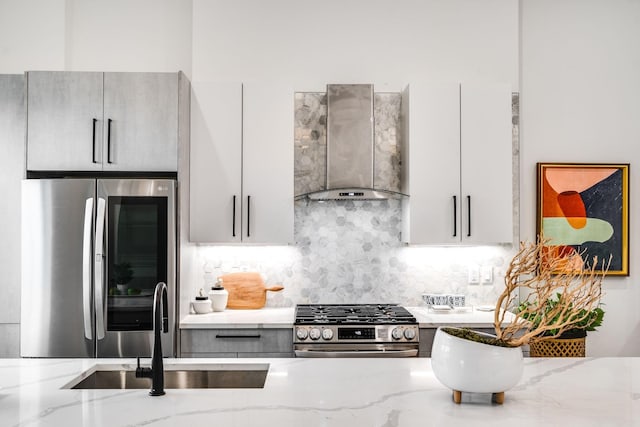 kitchen with backsplash, wall chimney range hood, sink, light stone countertops, and appliances with stainless steel finishes