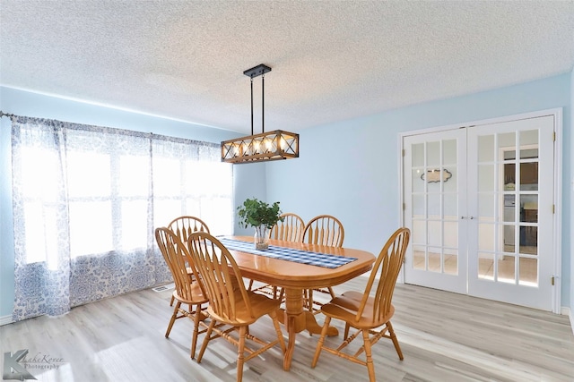 dining area with a textured ceiling, a notable chandelier, light hardwood / wood-style floors, and french doors