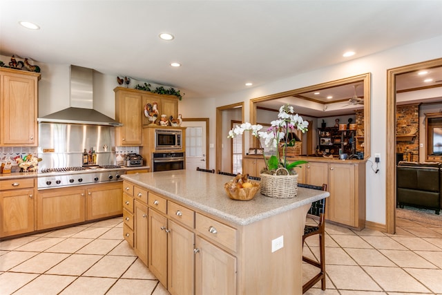 kitchen featuring light tile patterned floors, a kitchen island, wall chimney exhaust hood, stainless steel appliances, and a breakfast bar area