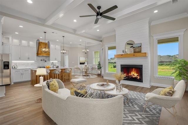 living room featuring beamed ceiling, ceiling fan with notable chandelier, a large fireplace, and light hardwood / wood-style floors