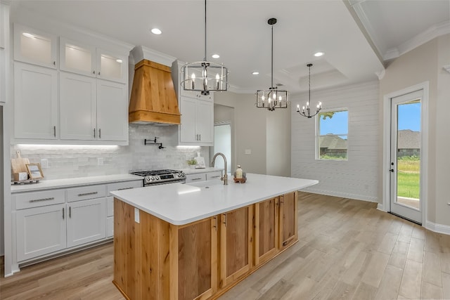 kitchen with hanging light fixtures, light hardwood / wood-style flooring, white cabinets, custom range hood, and stainless steel range with gas stovetop