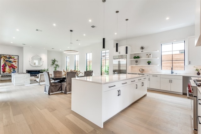 kitchen with light wood-type flooring, stainless steel appliances, white cabinets, a center island, and pendant lighting