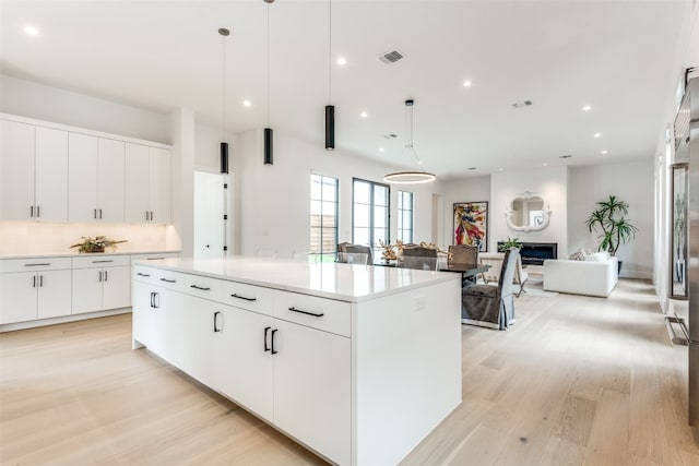 kitchen with hanging light fixtures, backsplash, light wood-type flooring, white cabinets, and a center island