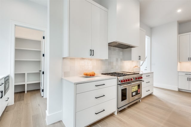 kitchen with backsplash, light wood-type flooring, white cabinetry, and range with two ovens