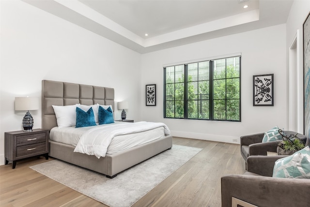 bedroom with a raised ceiling and light wood-type flooring