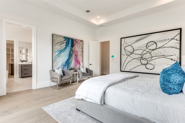 bedroom featuring a closet, connected bathroom, light hardwood / wood-style flooring, a spacious closet, and a raised ceiling