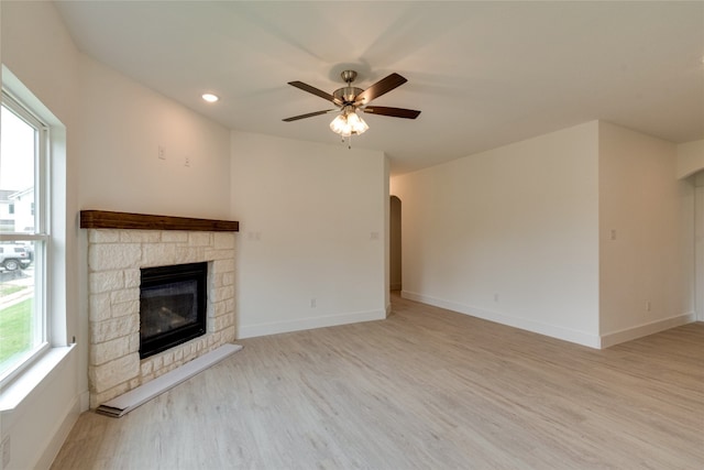 unfurnished living room with a stone fireplace, ceiling fan, and light hardwood / wood-style flooring