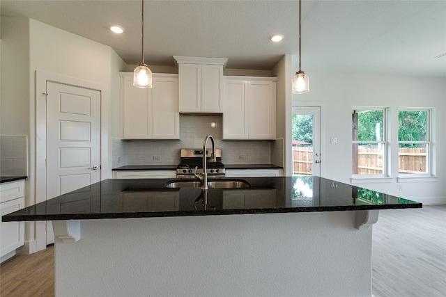 kitchen featuring decorative light fixtures, tasteful backsplash, white cabinets, a kitchen island with sink, and light wood-type flooring