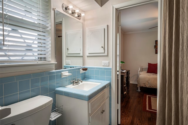 bathroom featuring tile walls, wood-type flooring, crown molding, vanity, and toilet