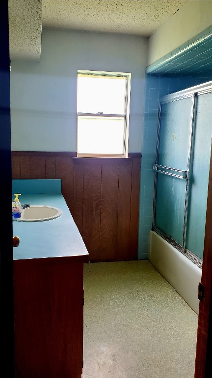 interior space with a textured ceiling, combined bath / shower with glass door, and vanity