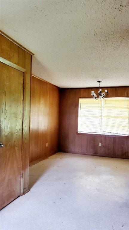 empty room with a textured ceiling, wooden walls, and a notable chandelier