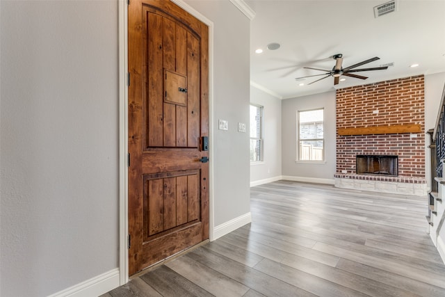 entryway featuring ornamental molding, ceiling fan, light hardwood / wood-style floors, and a fireplace