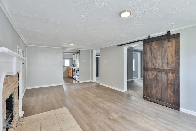 unfurnished living room featuring light hardwood / wood-style floors, crown molding, a barn door, and a textured ceiling