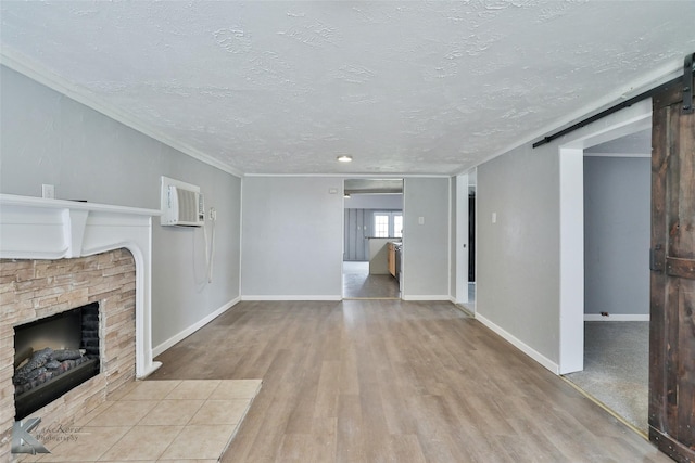 unfurnished living room with light hardwood / wood-style flooring, crown molding, a barn door, and a textured ceiling