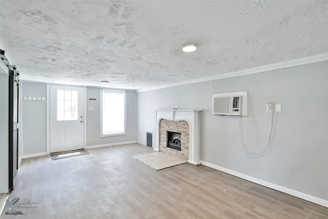 unfurnished living room with a wall mounted AC, hardwood / wood-style floors, a textured ceiling, and a barn door