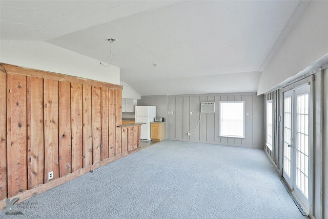 unfurnished living room with wood walls, a wall mounted air conditioner, light carpet, and lofted ceiling