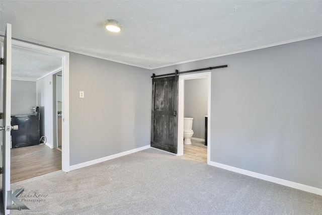 unfurnished bedroom featuring light carpet, ensuite bathroom, a barn door, and ornamental molding