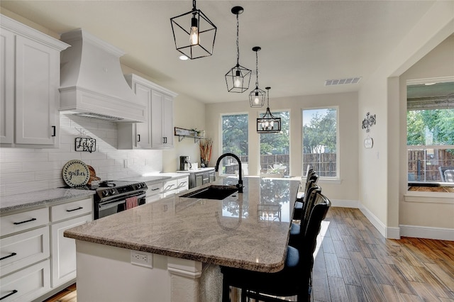 kitchen featuring custom range hood, a center island with sink, a kitchen bar, and tasteful backsplash