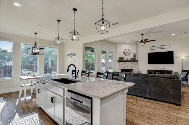 kitchen featuring white cabinetry, a center island with sink, hanging light fixtures, and sink