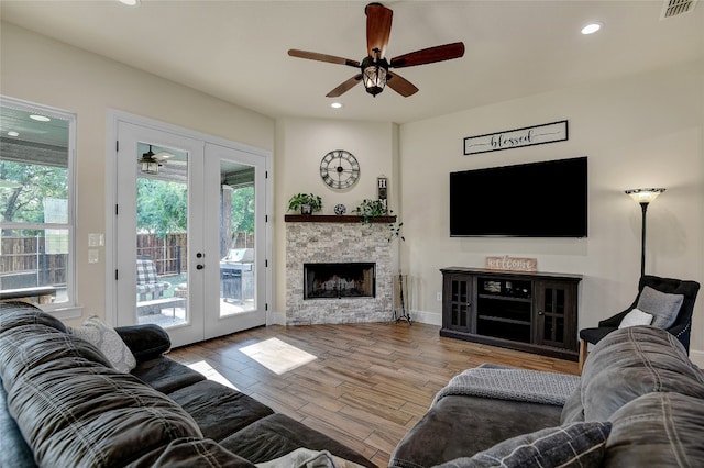 living room featuring french doors, light hardwood / wood-style floors, ceiling fan, and a fireplace