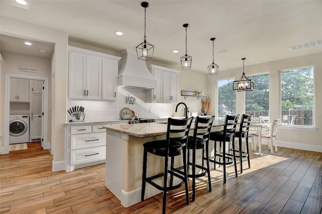 kitchen featuring decorative light fixtures, backsplash, washer / dryer, white cabinets, and custom range hood