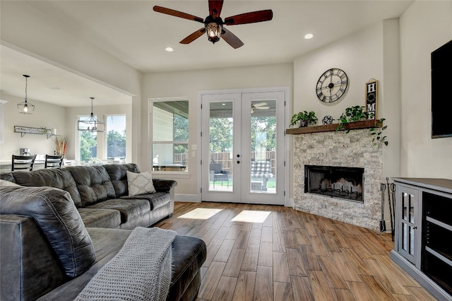 living room featuring french doors, ceiling fan with notable chandelier, a fireplace, and light hardwood / wood-style flooring