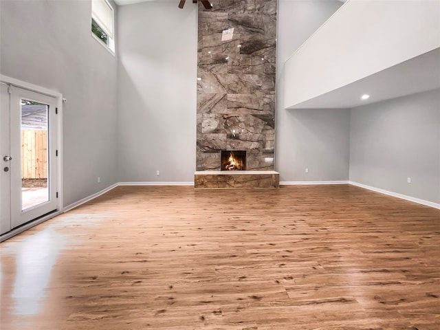 unfurnished living room featuring a high ceiling, a stone fireplace, and light hardwood / wood-style floors