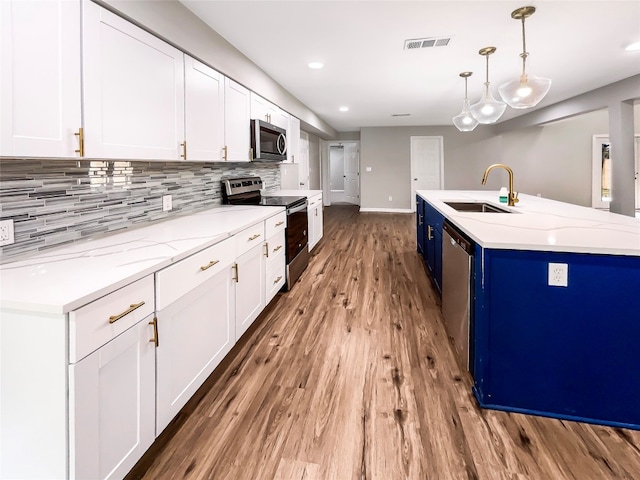 kitchen with sink, appliances with stainless steel finishes, decorative light fixtures, white cabinetry, and hardwood / wood-style flooring