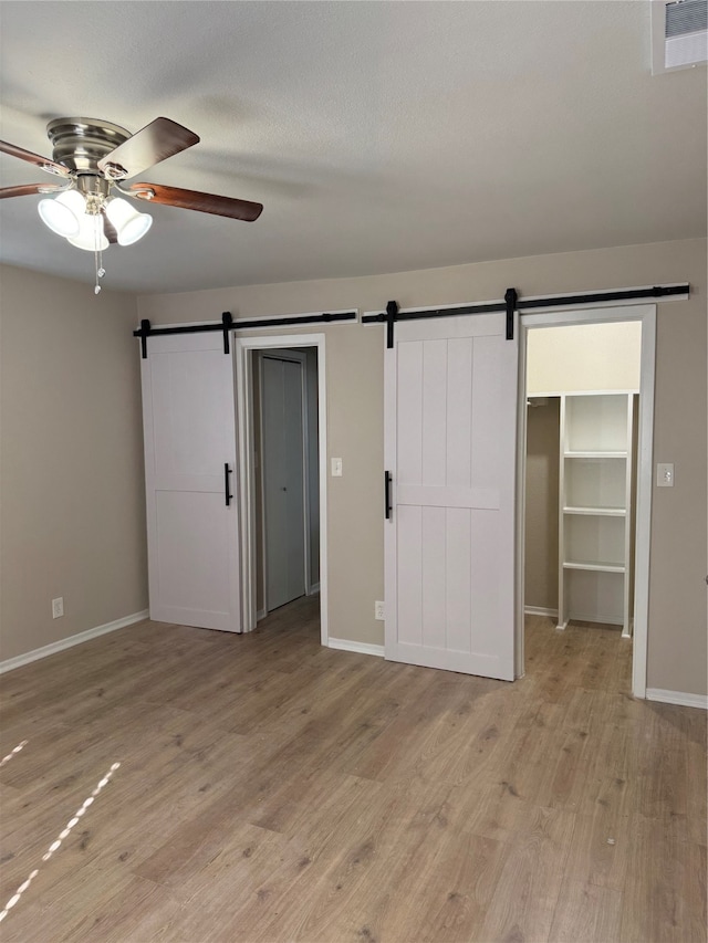 unfurnished bedroom with ceiling fan, a barn door, light hardwood / wood-style flooring, a walk in closet, and a closet