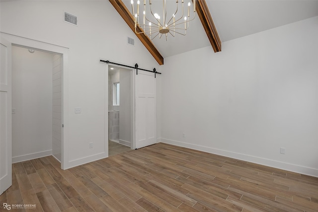 unfurnished bedroom with a chandelier, beam ceiling, a barn door, and high vaulted ceiling