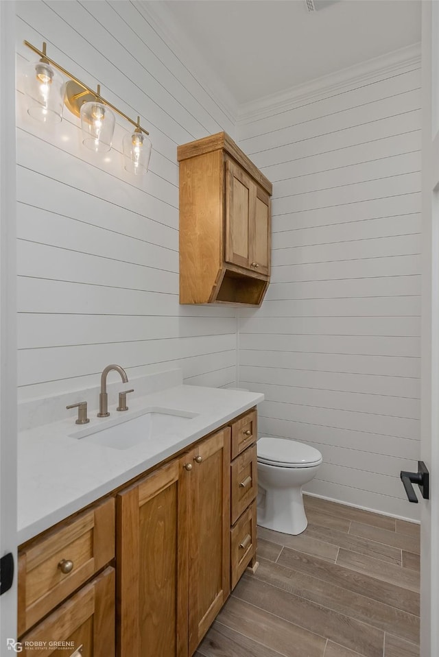 bathroom featuring wood walls, vanity, ornamental molding, and toilet