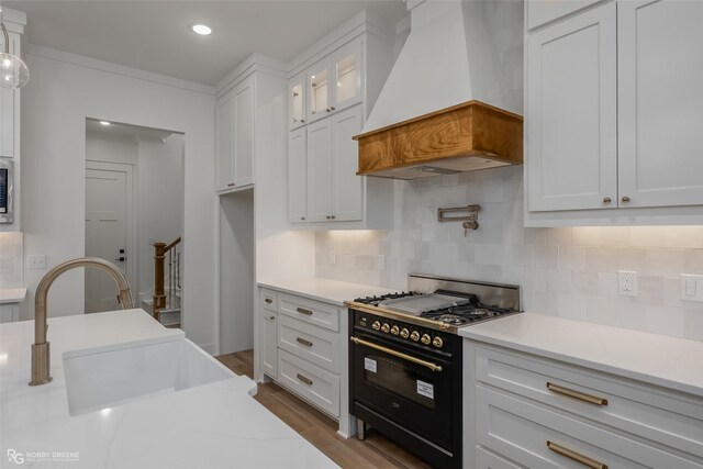 kitchen featuring tasteful backsplash, custom range hood, sink, range with two ovens, and white cabinetry