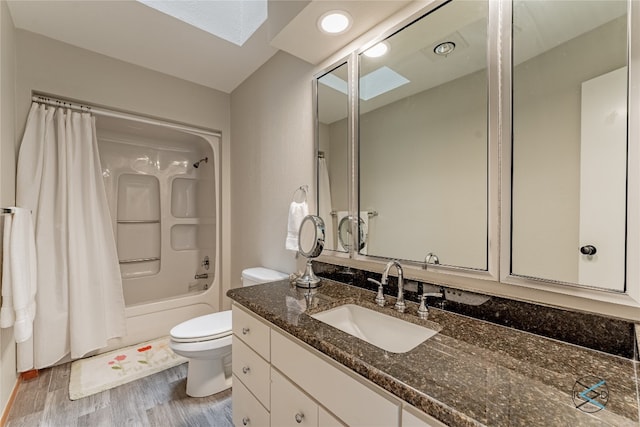 full bathroom featuring hardwood / wood-style floors, a skylight, shower / tub combo with curtain, vanity with extensive cabinet space, and toilet