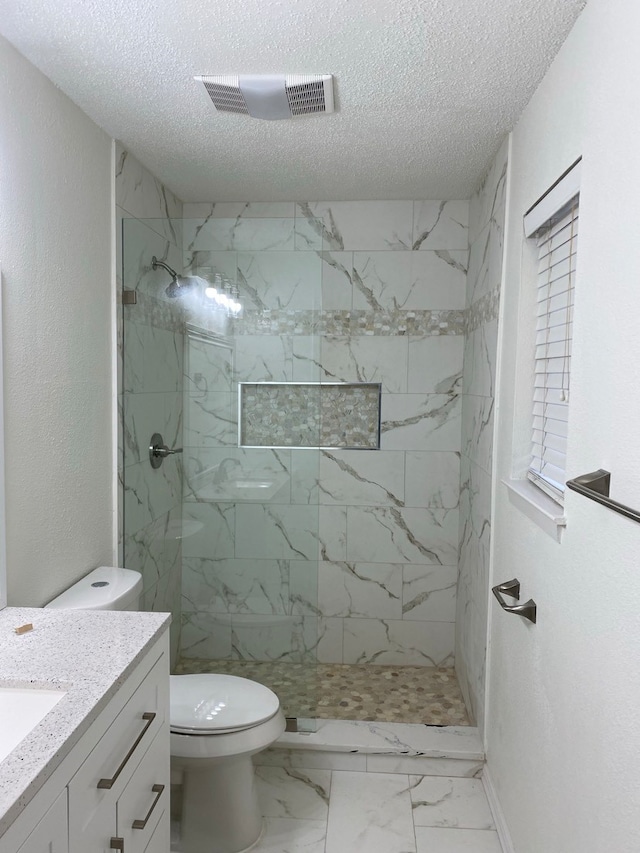 bathroom with vanity, toilet, a textured ceiling, and tiled shower