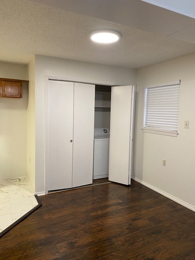 unfurnished bedroom with a closet, washer / dryer, a textured ceiling, and dark hardwood / wood-style flooring