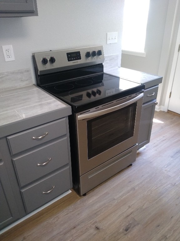 kitchen featuring gray cabinetry, light hardwood / wood-style floors, and stainless steel electric range oven