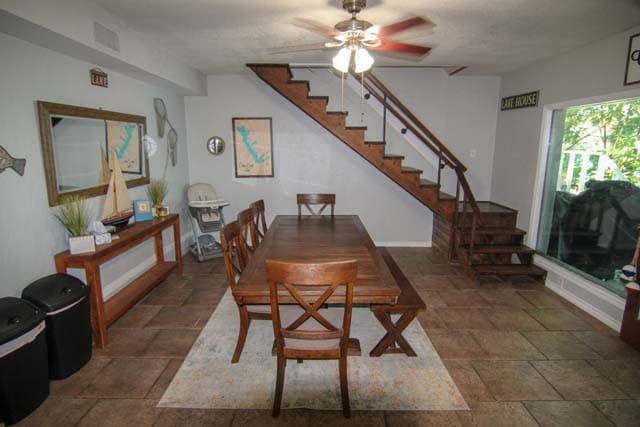 dining area featuring stone finish flooring, visible vents, ceiling fan, and stairway