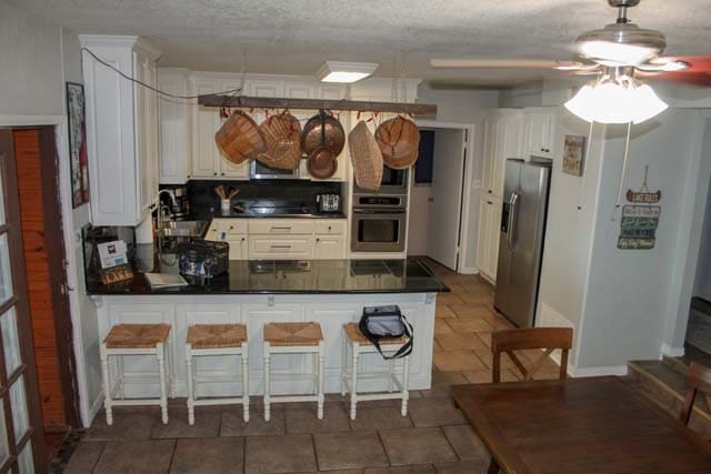 kitchen featuring a peninsula, a sink, white cabinets, appliances with stainless steel finishes, and dark countertops