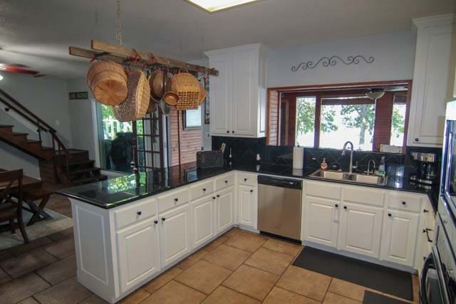 kitchen with tasteful backsplash, dark countertops, stainless steel dishwasher, a sink, and a peninsula