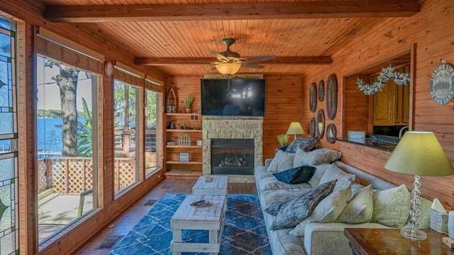 living area with beamed ceiling, wood walls, an outdoor stone fireplace, and wooden ceiling