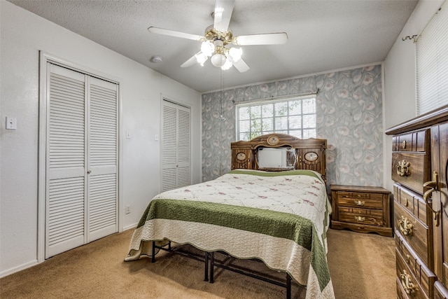 carpeted bedroom with a textured ceiling, ceiling fan, and multiple closets