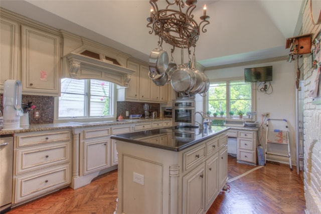 kitchen with an island with sink, cream cabinetry, tasteful backsplash, and parquet floors