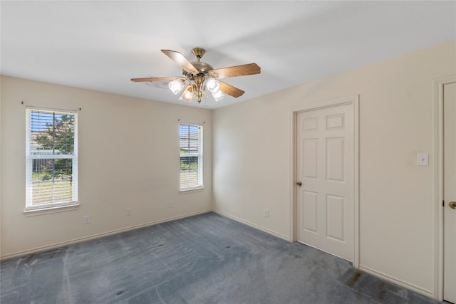 spare room featuring dark colored carpet, ceiling fan, and a healthy amount of sunlight