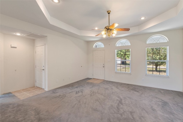 empty room with light carpet, a tray ceiling, and ceiling fan