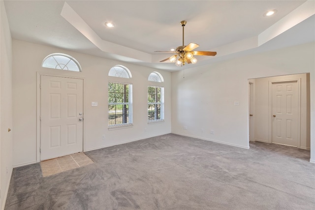 carpeted foyer entrance with ceiling fan and a tray ceiling