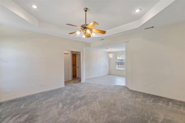 carpeted empty room with a raised ceiling and ceiling fan