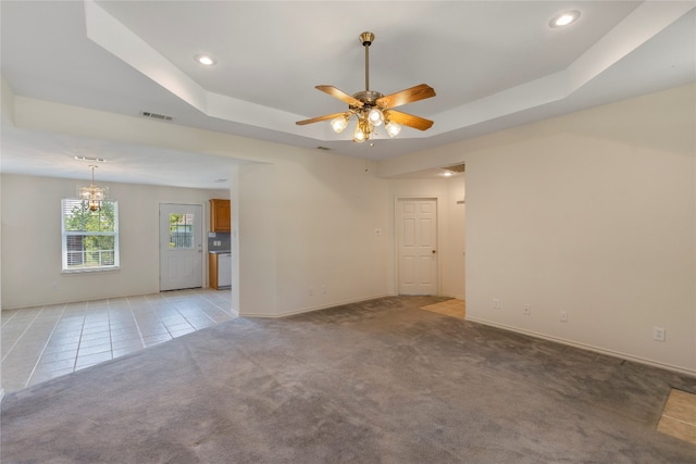 carpeted spare room with a tray ceiling and ceiling fan with notable chandelier