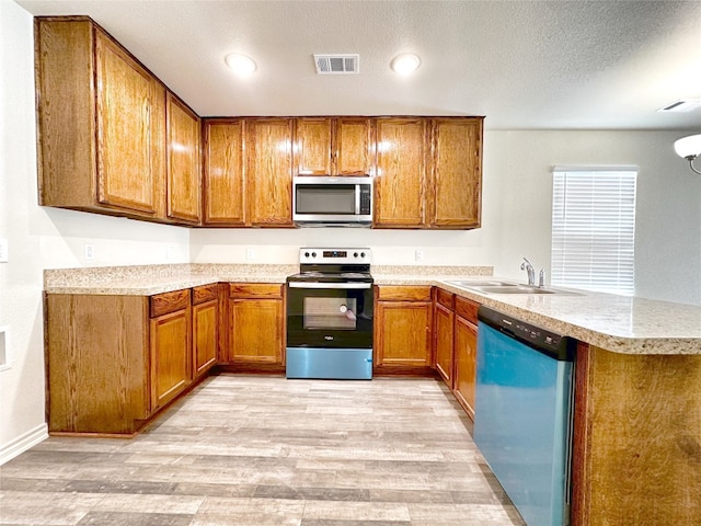 kitchen with kitchen peninsula, sink, appliances with stainless steel finishes, light hardwood / wood-style floors, and a textured ceiling