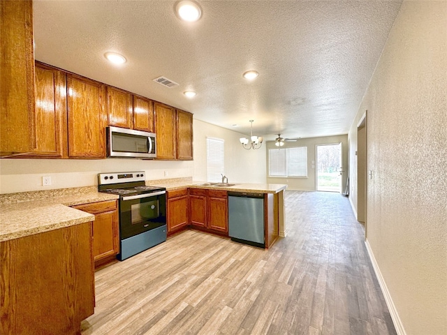 kitchen featuring pendant lighting, sink, appliances with stainless steel finishes, light hardwood / wood-style floors, and ceiling fan with notable chandelier