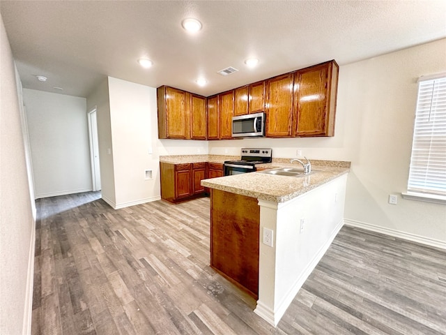 kitchen featuring kitchen peninsula, stainless steel appliances, sink, and light hardwood / wood-style flooring